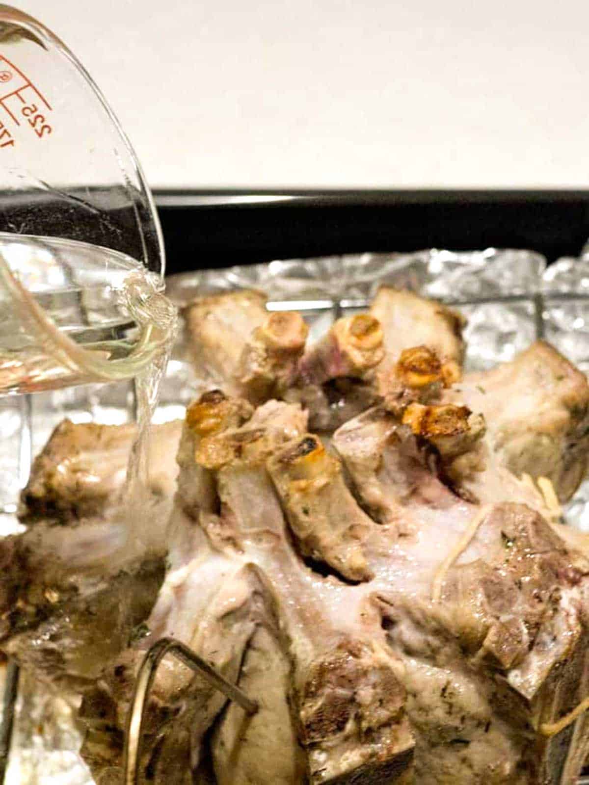 Adding some vermouth to the partially cooked crown roast of pork.