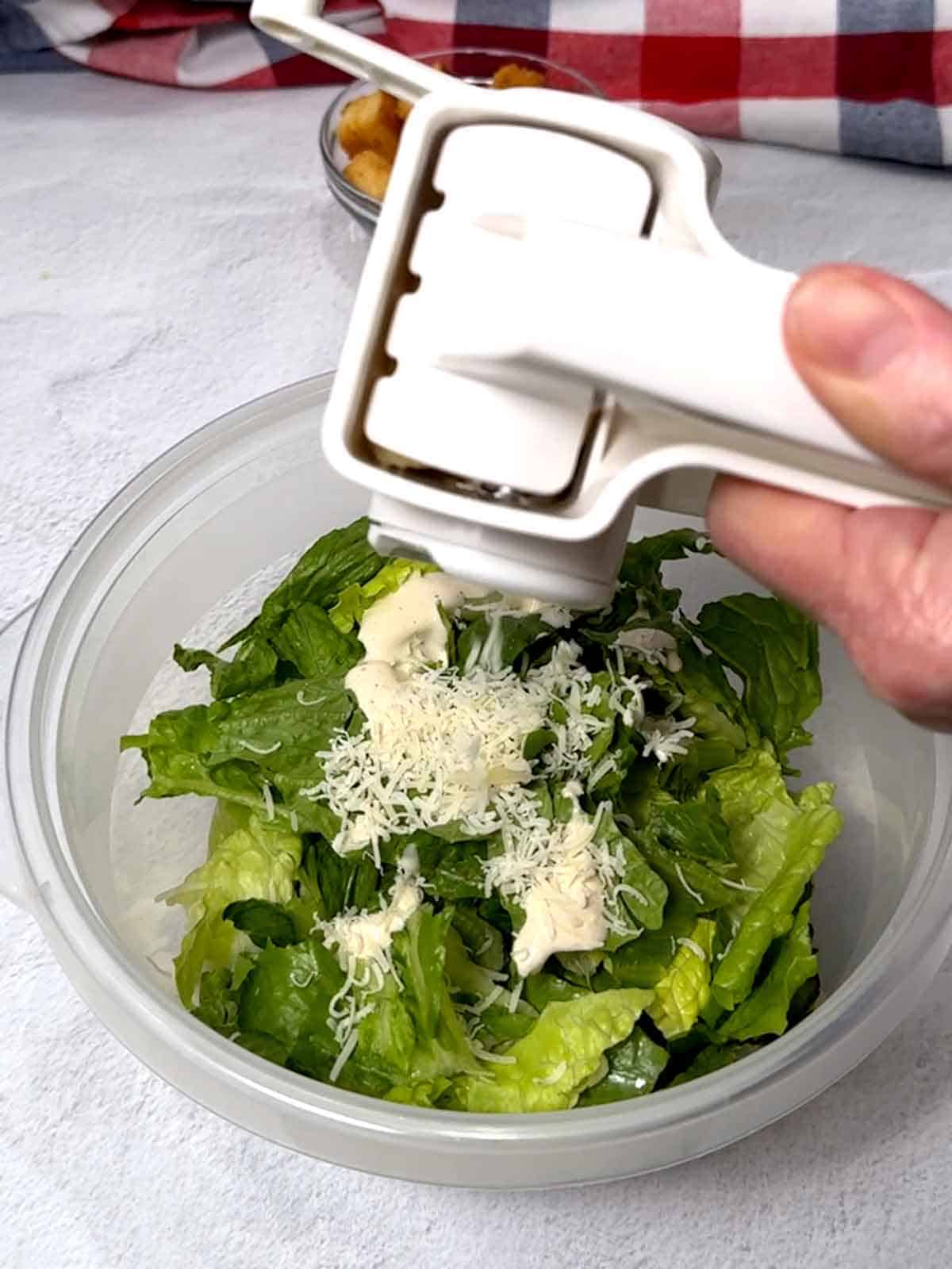 Adding freshly grated Parmesan cheese to the Romaine lettuce and dressing.