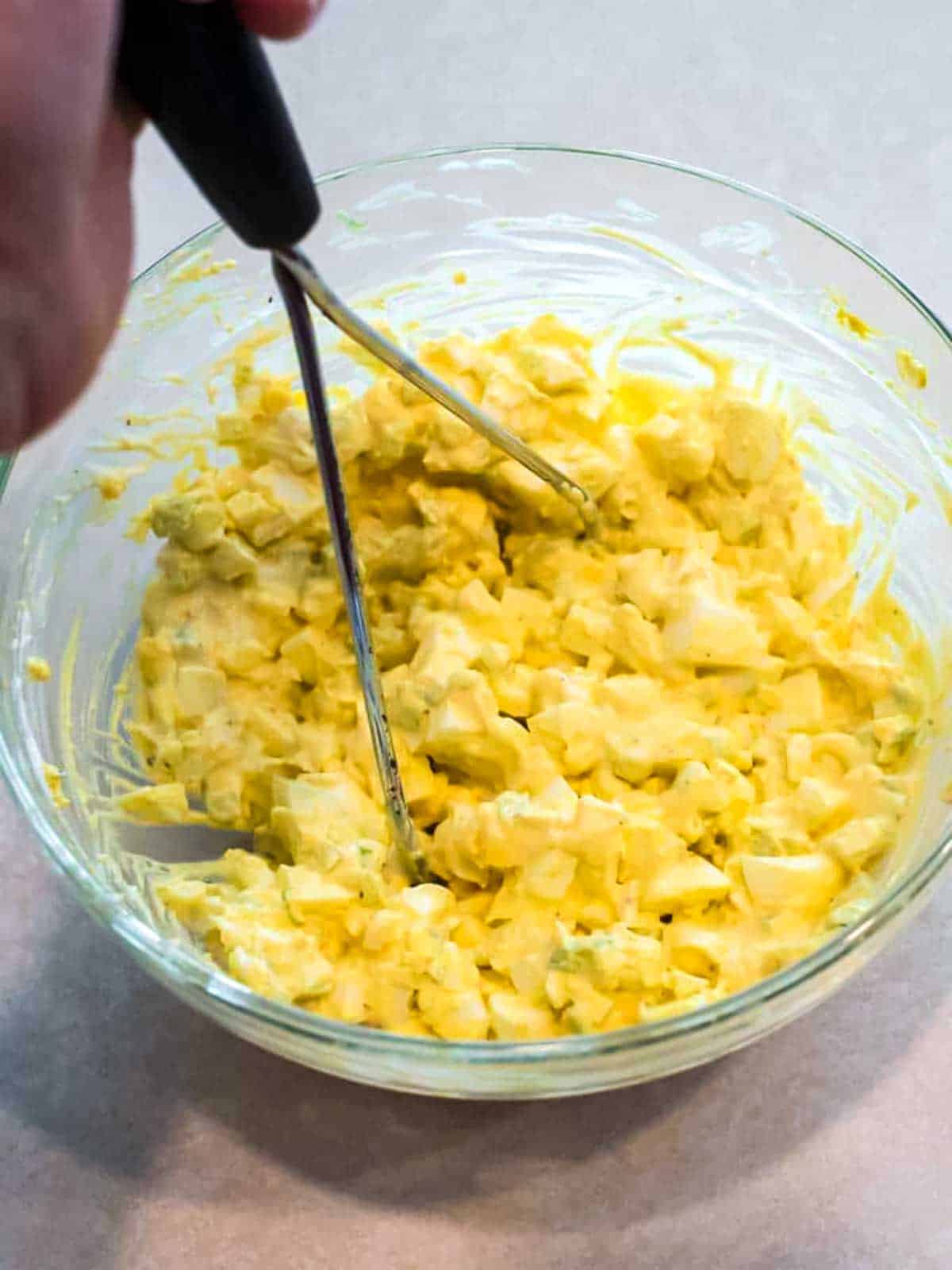 Using a potato masher to mix all of the egg salad ingredients together.
