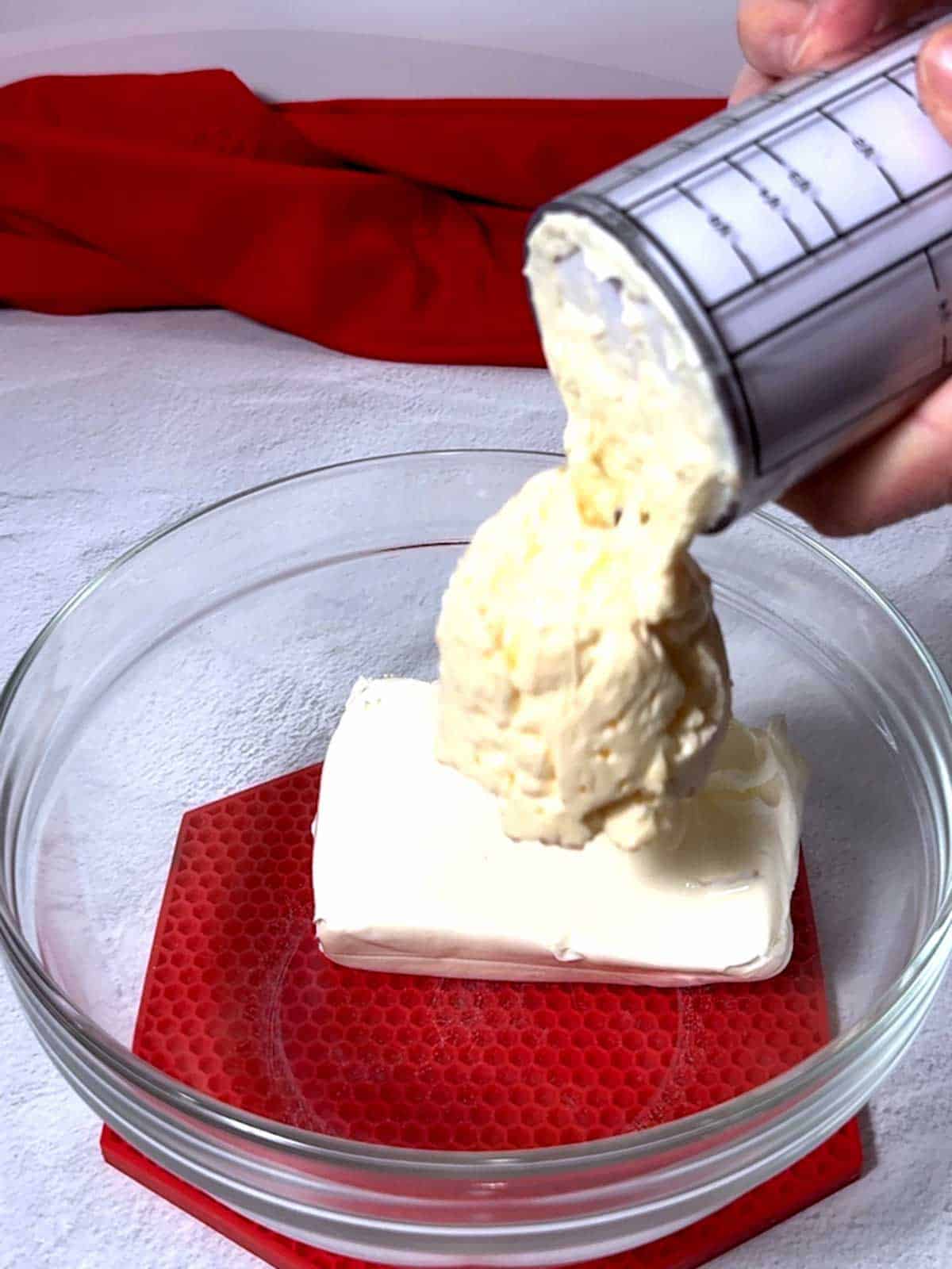 Adding mayonnaise to cream cheese in a bowl.