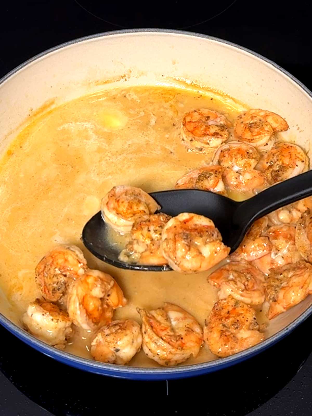 Removing the shrimp from the sauce with a slotted spoon.