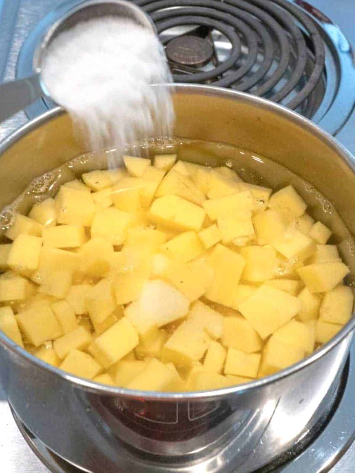 Adding salt to the potatoes in a pot of water on the stove.