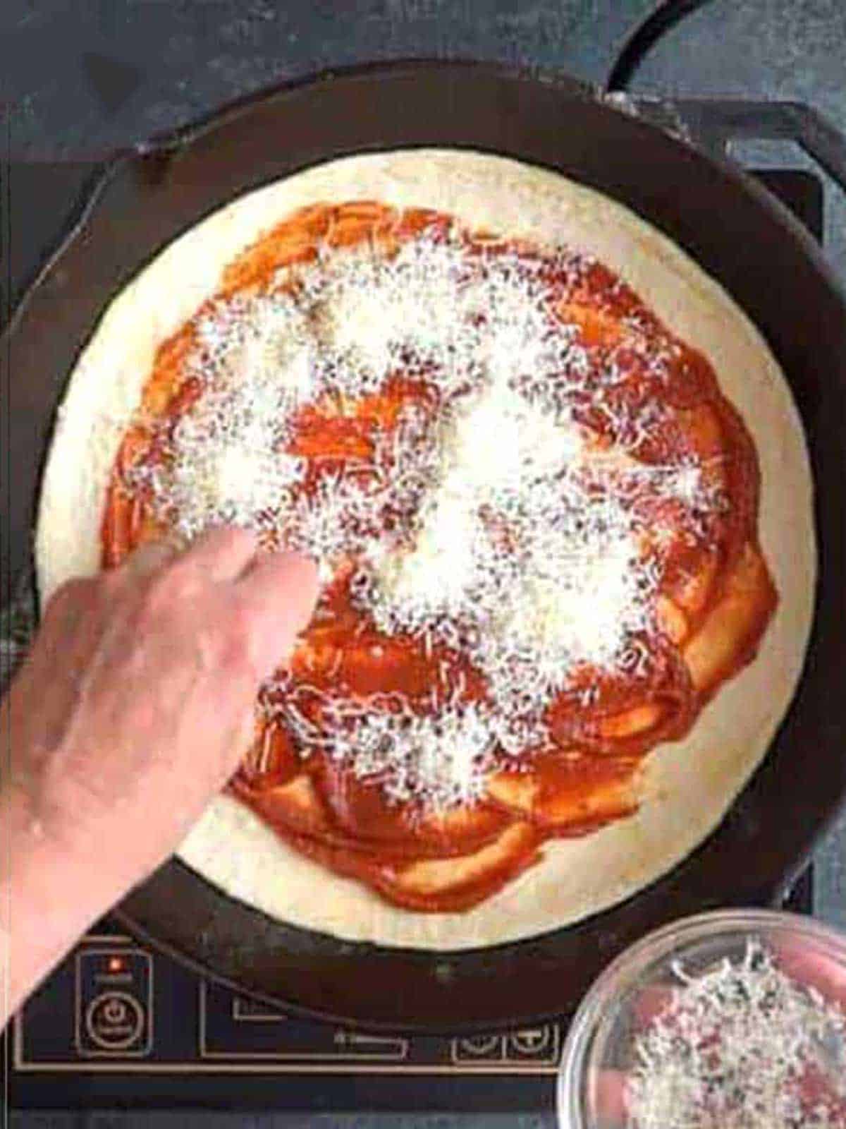 Adding parmesan cheese to the pizza in the cast iron skillet.