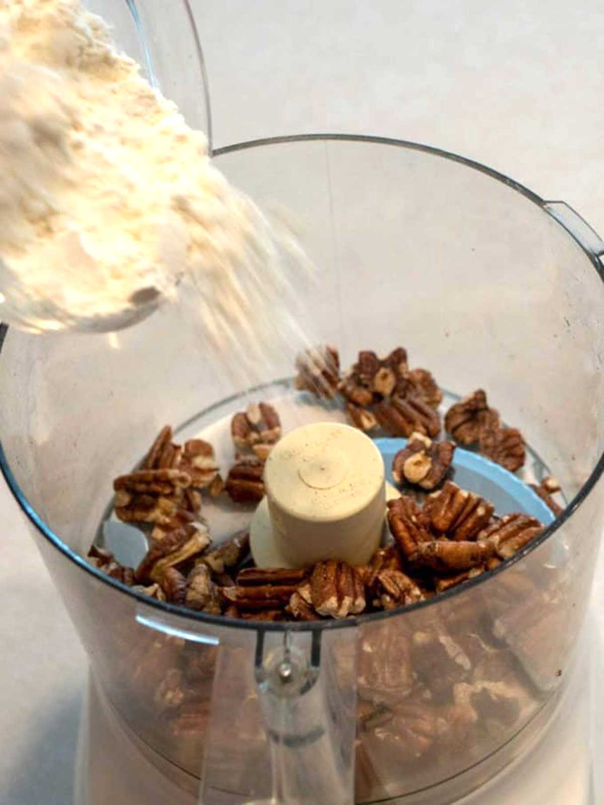 Adding flour to pecans in a food processor.