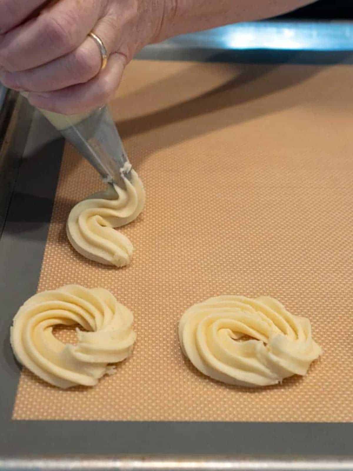 Piping cookie dough onto a silicone-lined baking sheet.