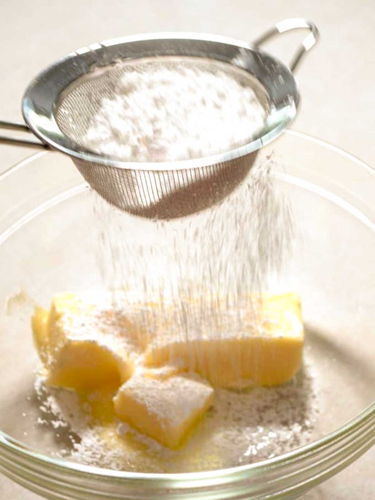 Sifting confectioners' sugar into bowl with butter.