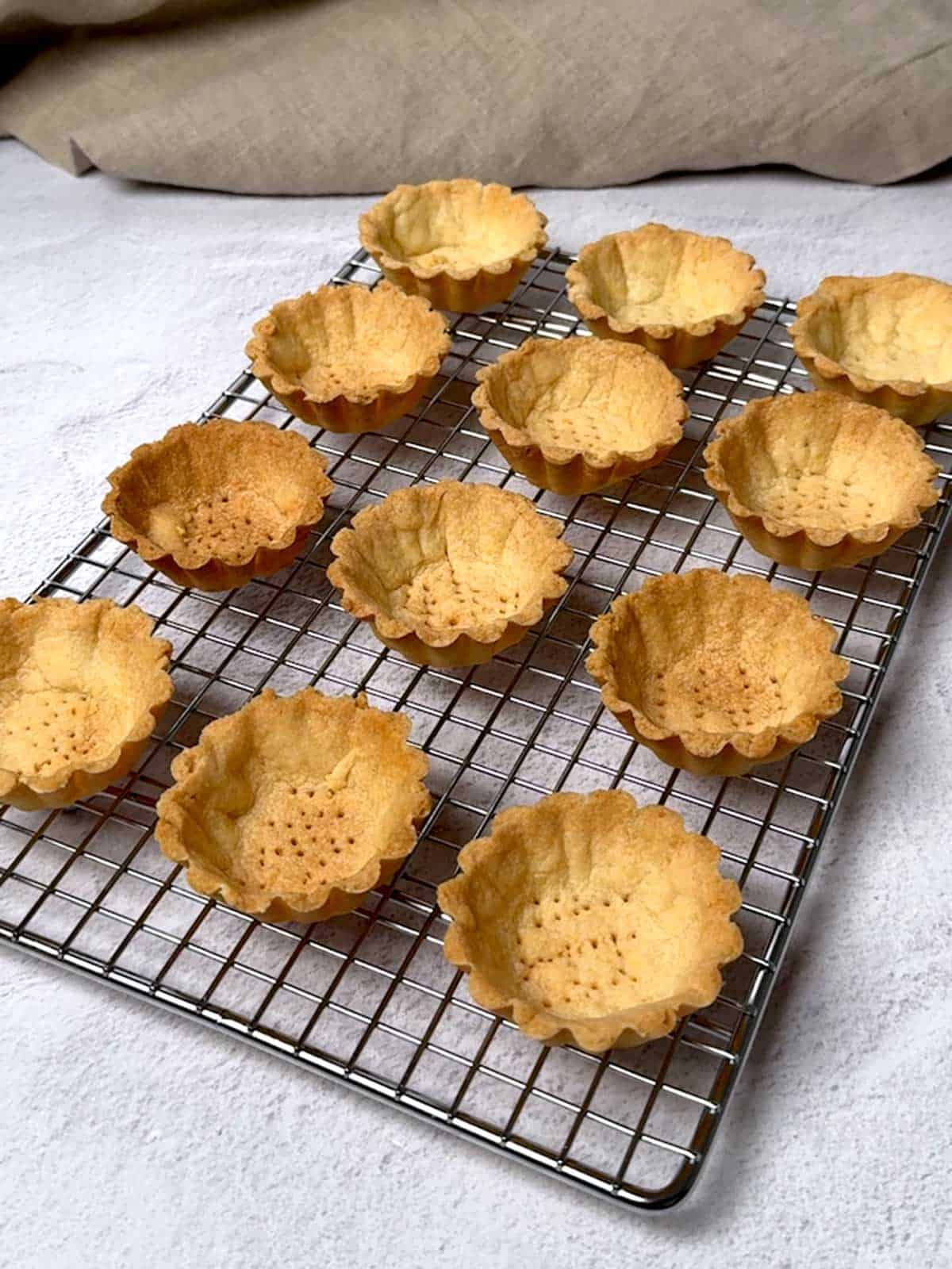 Pâte Sucrée mini tart shells cooling on a wire rack.