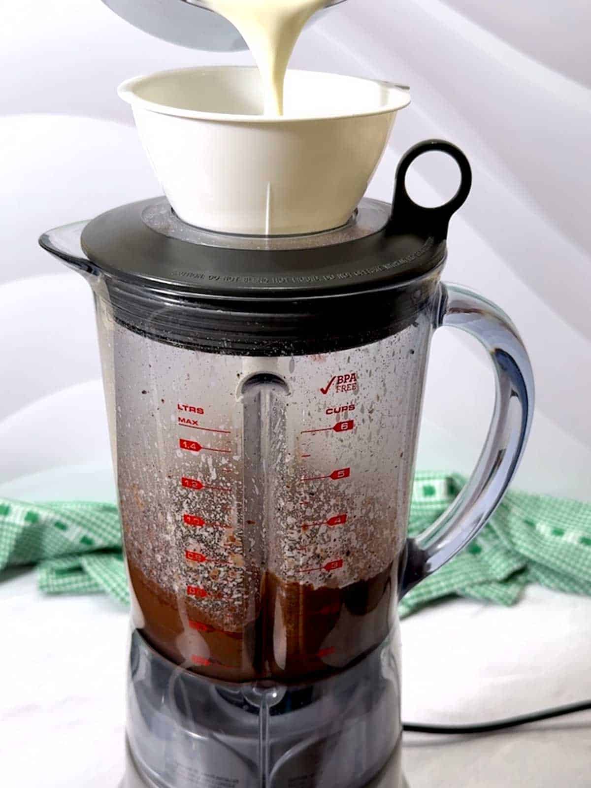 Adding hot cream to the blender with the chocolate mixture.