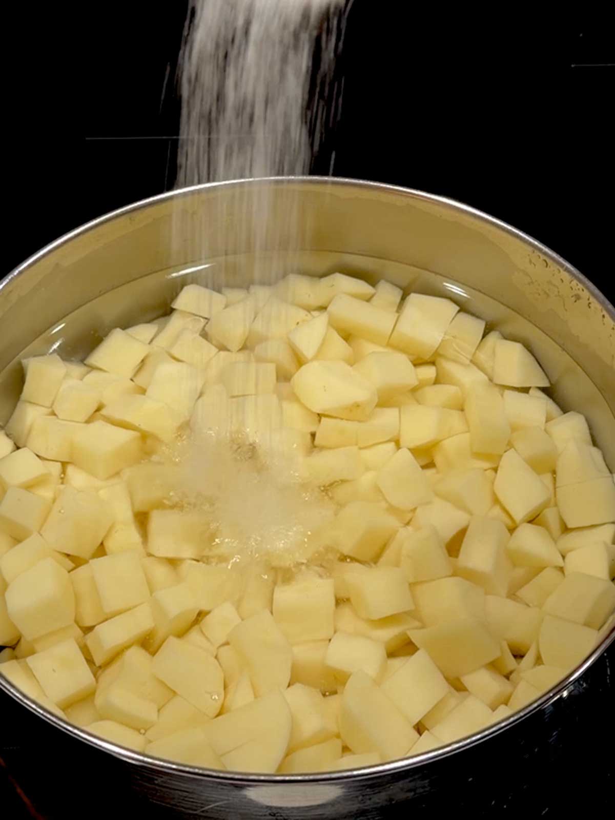 Adding salt to the water with the potatoes.