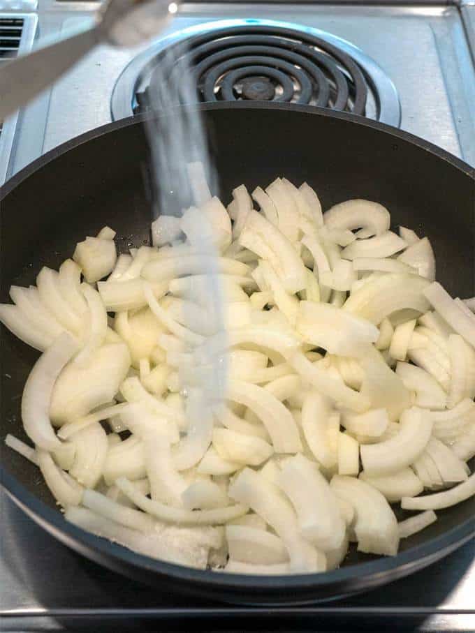 Adding salt to the onions in the skillet.