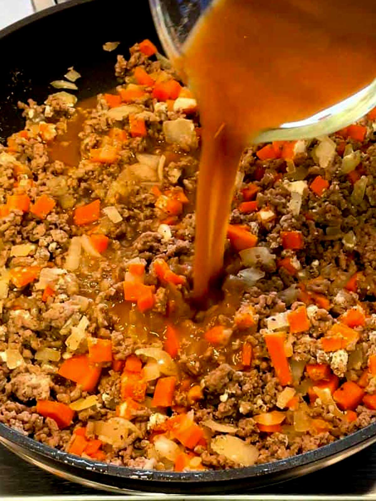 Adding broth to the cottage pie ingredients.