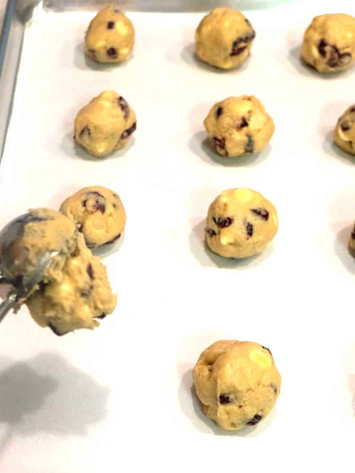 Dropping cookie dougn onto parchment lined baking sheet.