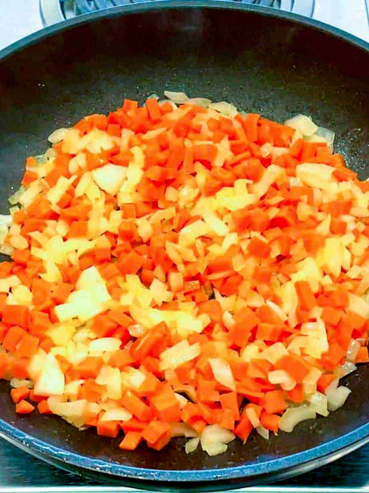 Cooking onions and carrots in a pan.