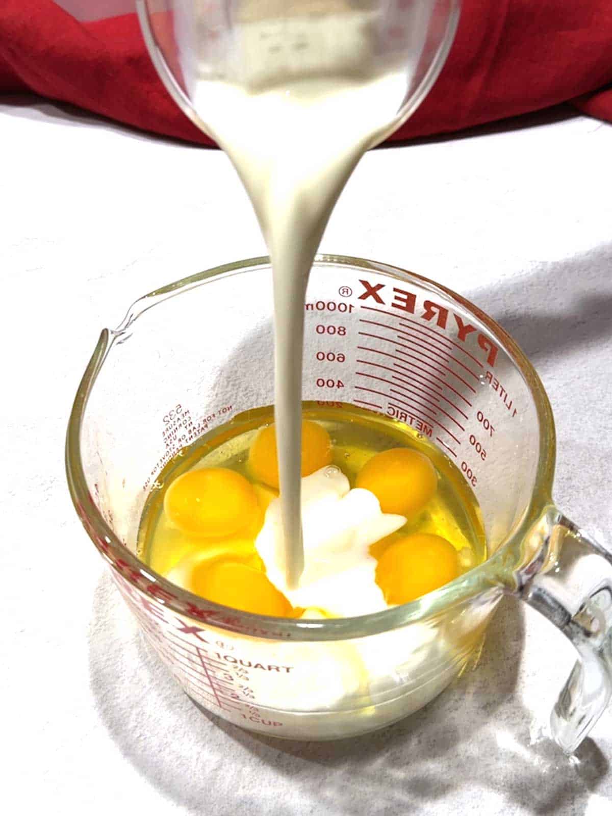 Adding milk to the eggs in a large measuring cup.