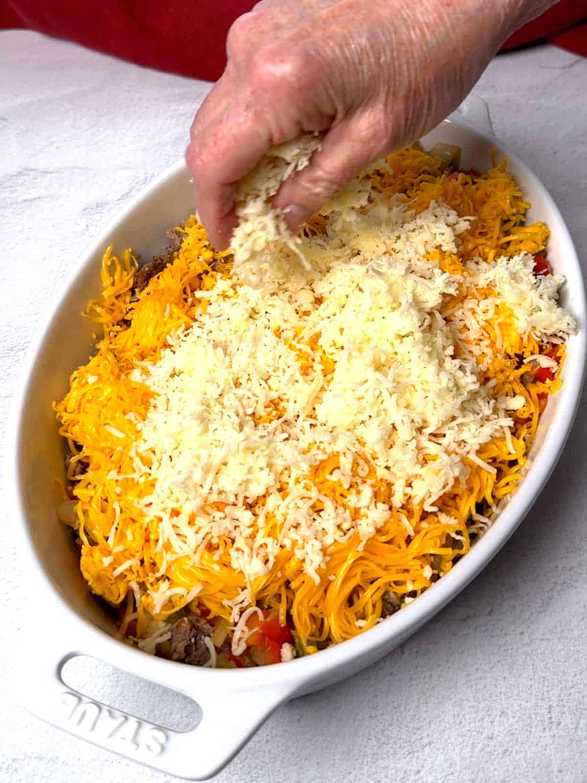 Adding shredded mozzarella cheese to the casserole.