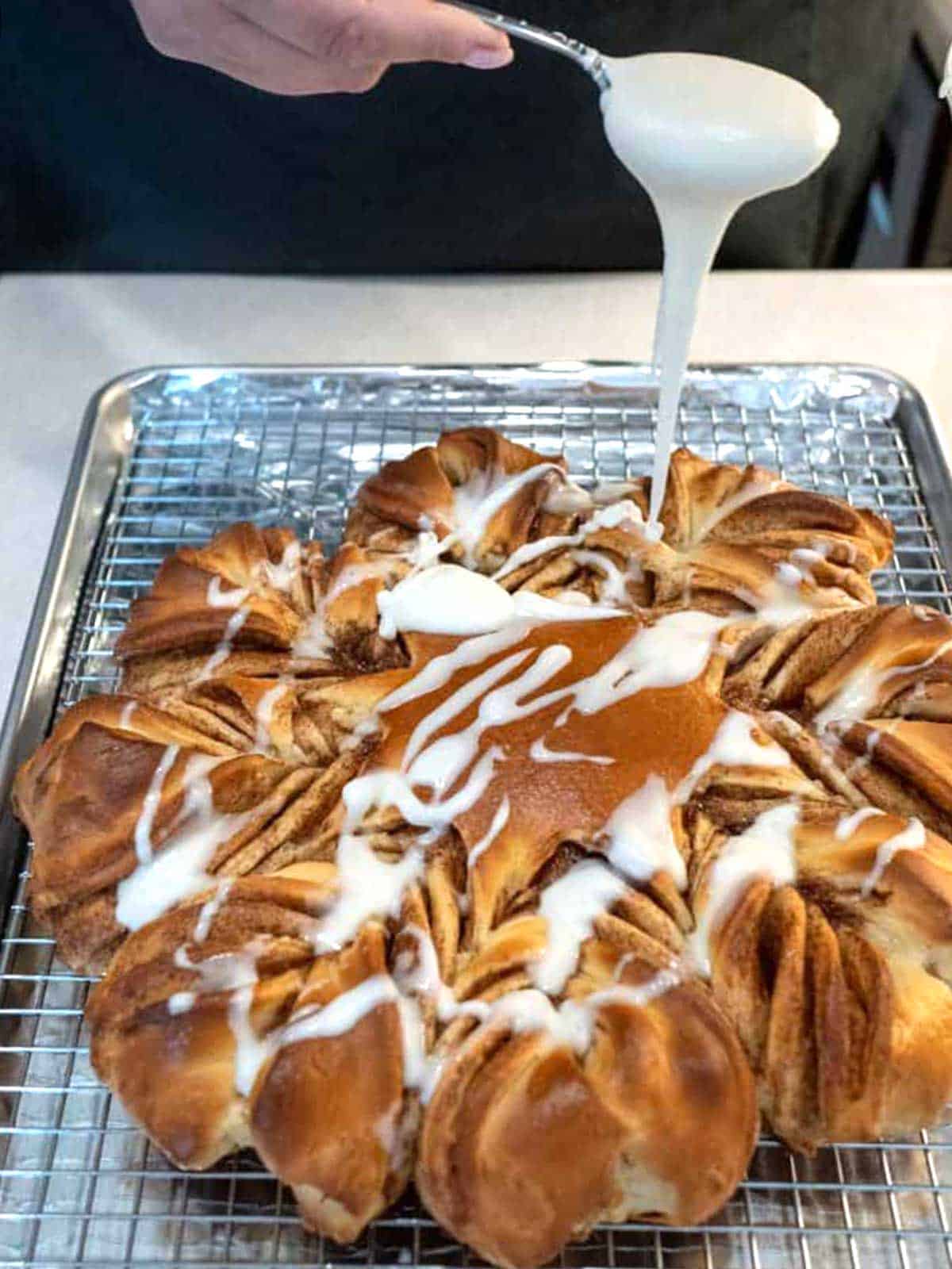 Drizzling icing over the hot cinnamon snowflake bread.