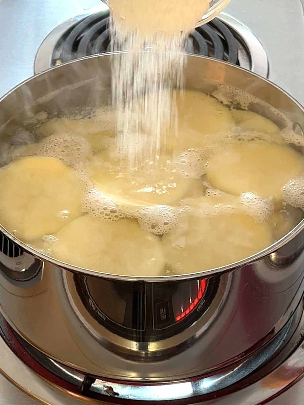 Adding salt to boiling water with potatoes.