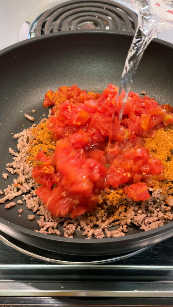 Adding water to ground beef, taco seasoning and Rotel tomatoes.