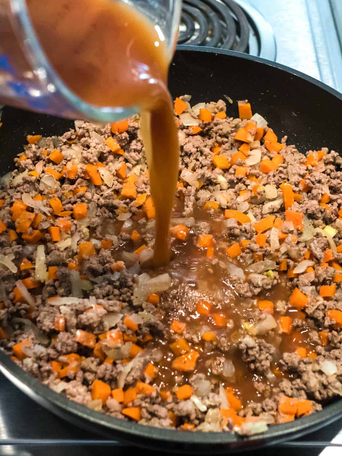 Adding beef broth to meat and vegetable mixture.