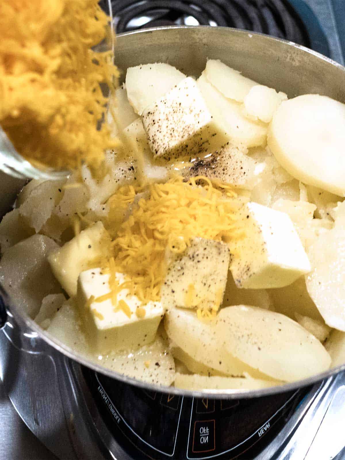 Adding cheese to the potatoes with butter, milk and pepper.