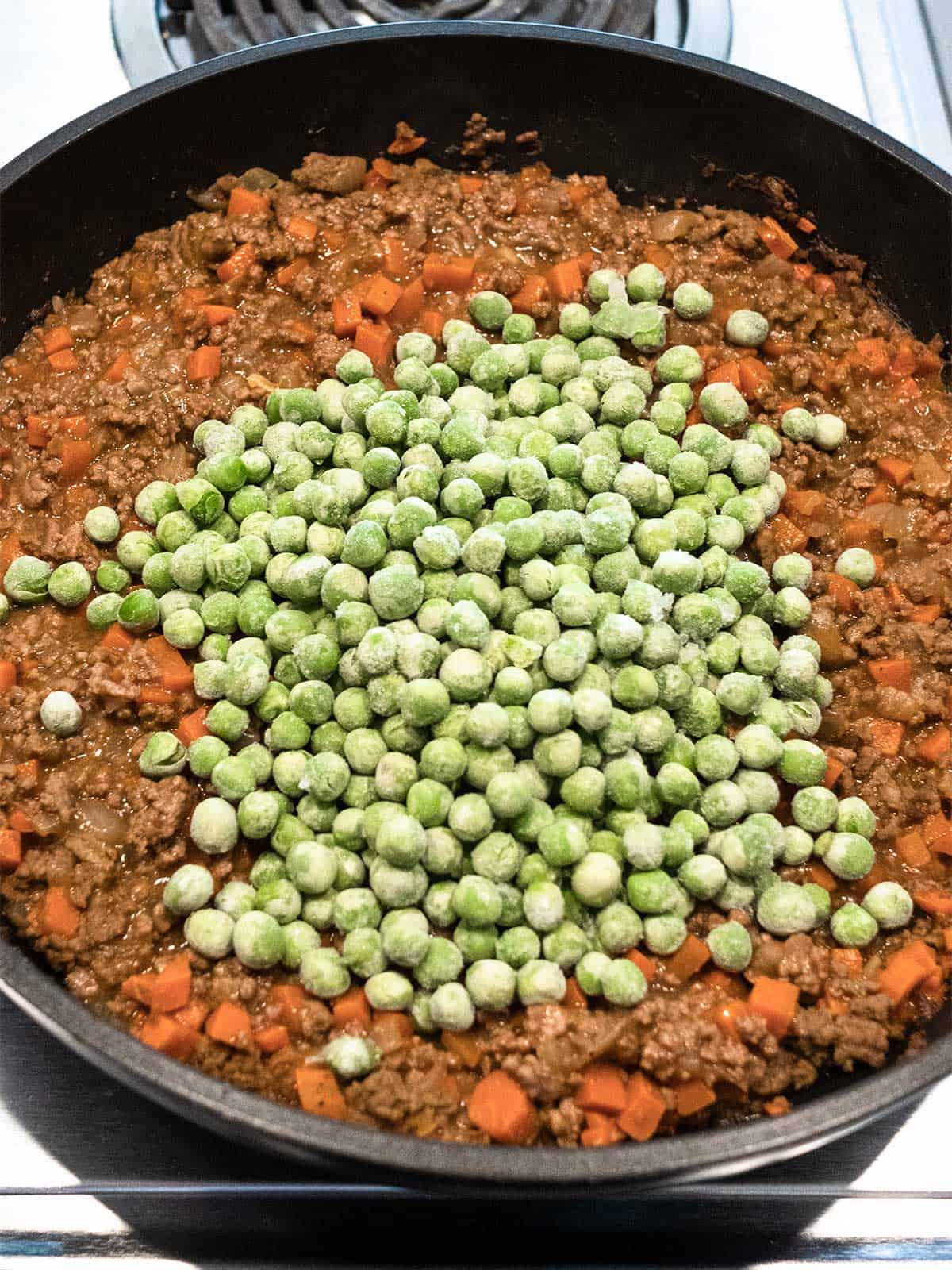 Adding green peas to the meat mixture.