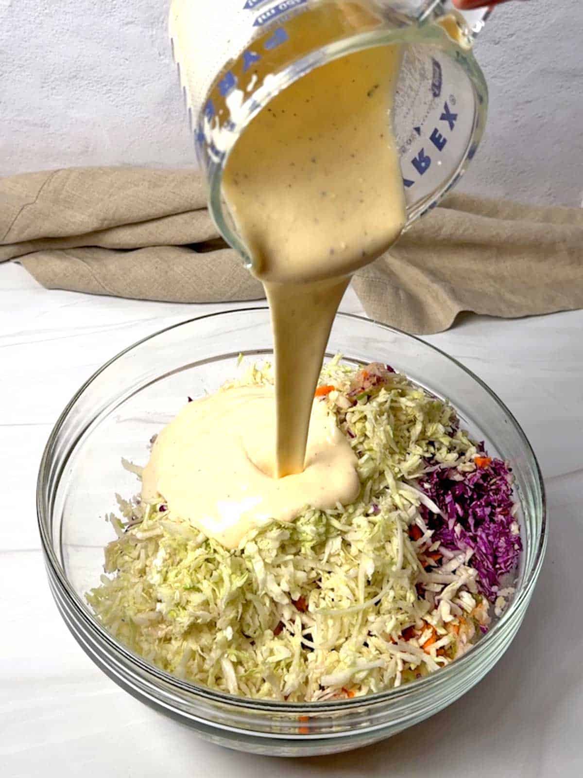 Adding coleslaw dressing to the veggies.