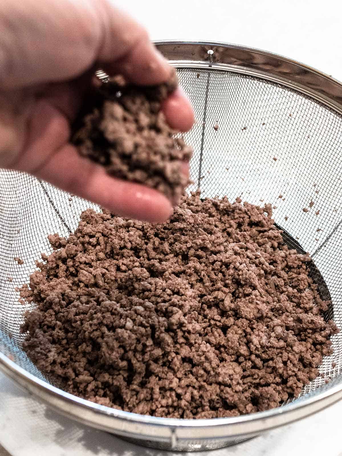 Crumbling cooked ground beef into smaller pieces.