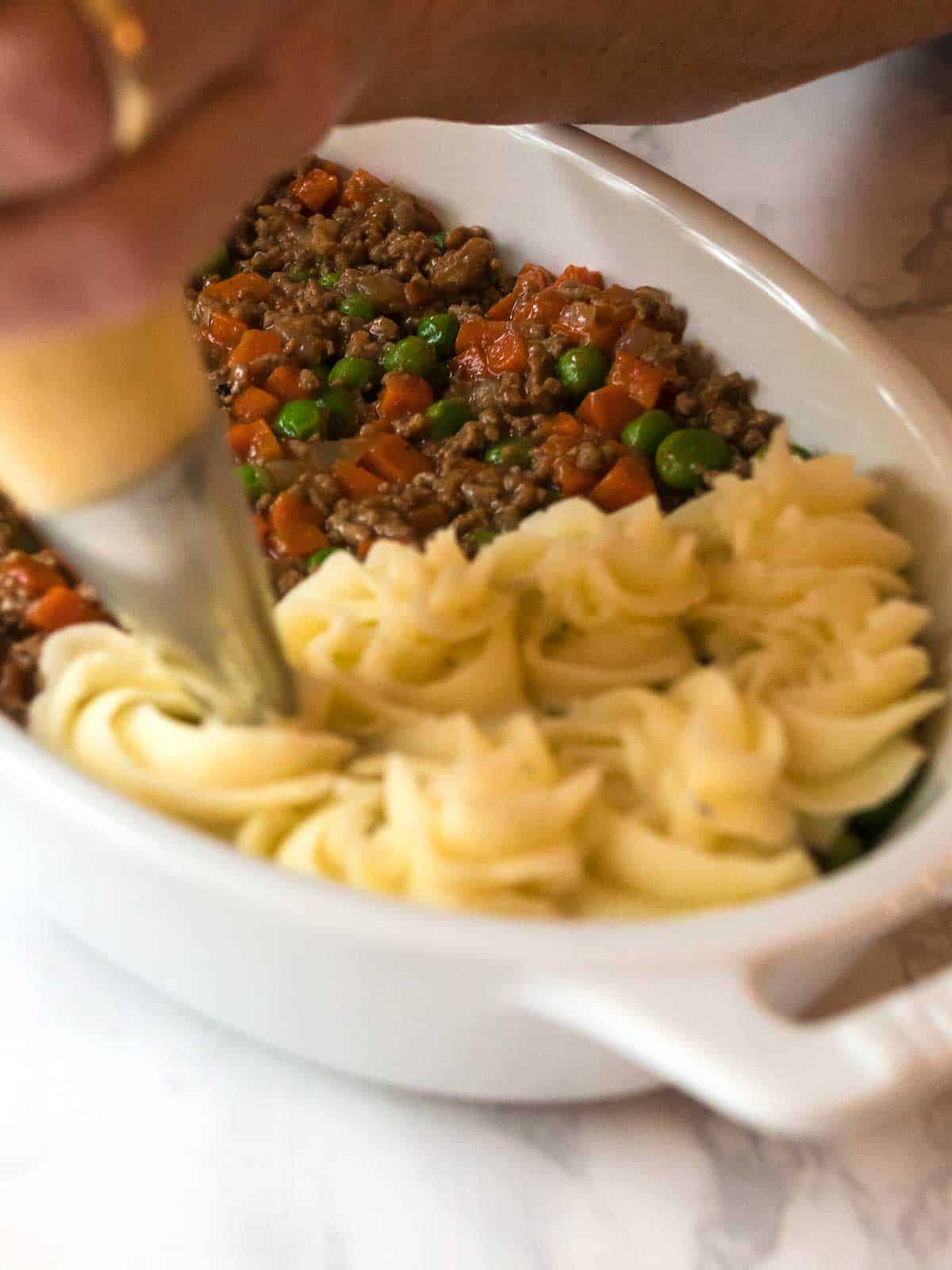 Piping mashed potatoes onto meat mixture.