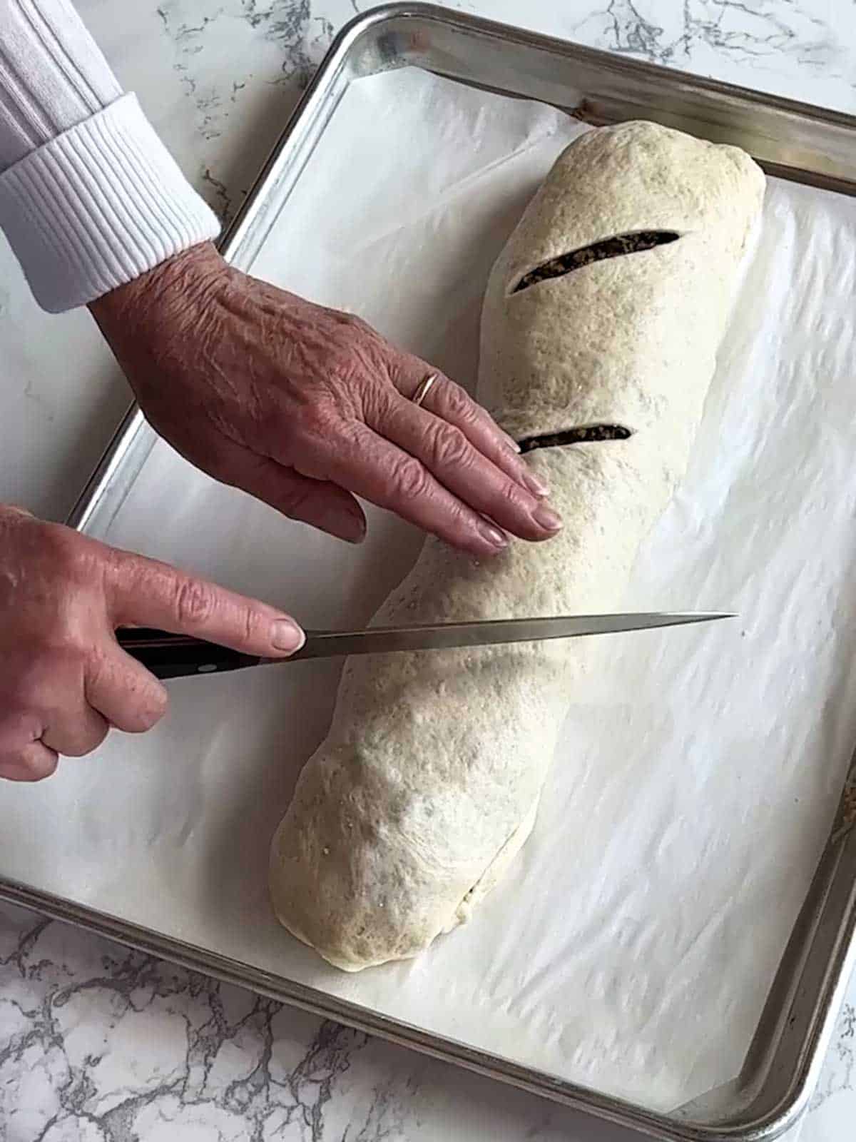 Cutting slits on the top of the sausage bread before baking it.