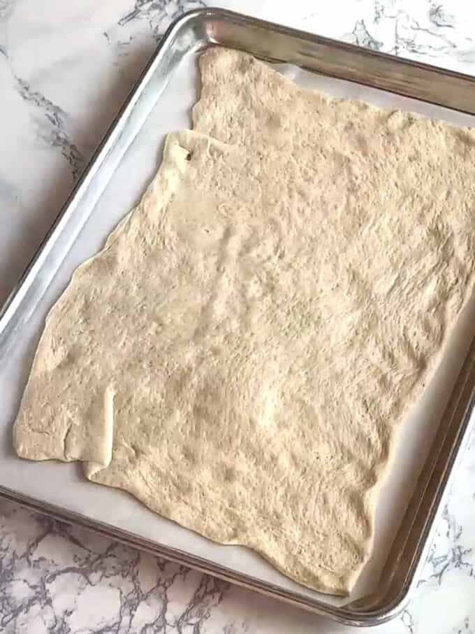 Pizza crust on parchment lined baking sheet.