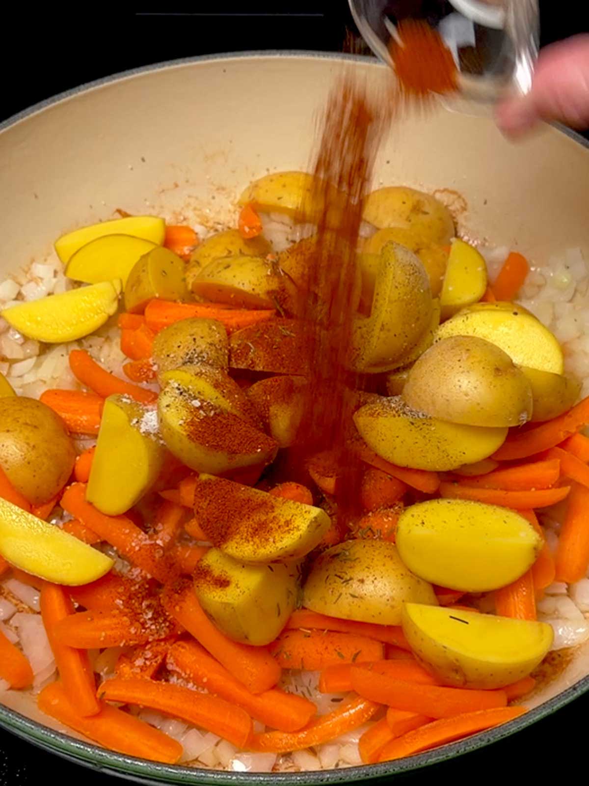 Adding paprika to the veggies in the braiser.