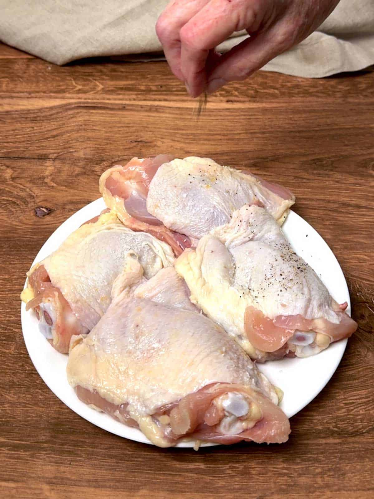 Adding pepper to the chicken thighs.