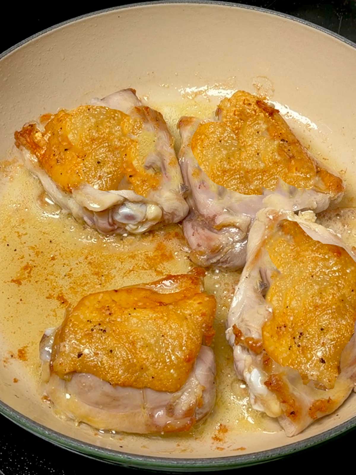 Browned chicken thighs in a braiser.