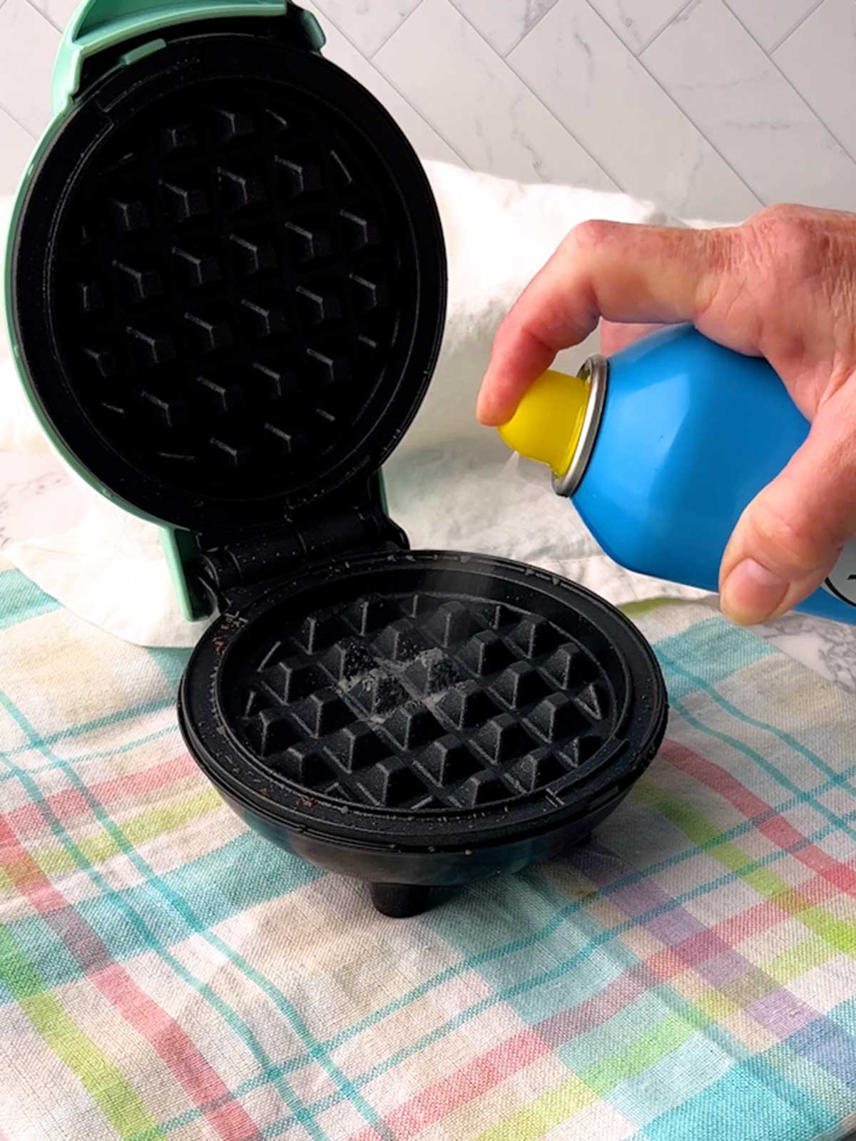 Spraying vegetable oil into mini waffle maker.
