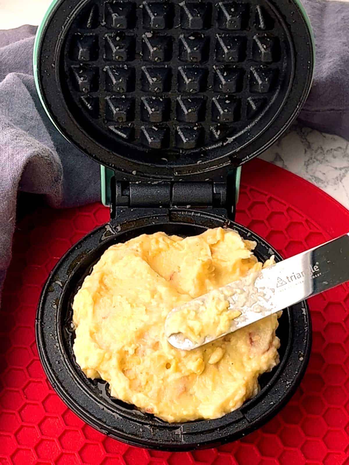 Spreading potato waffle batter on bottom of mini waffle maker.