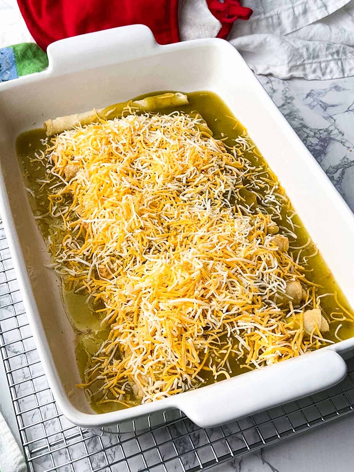 Taquitos topped with green enchilada sauce and shredded Mexican blend cheese.