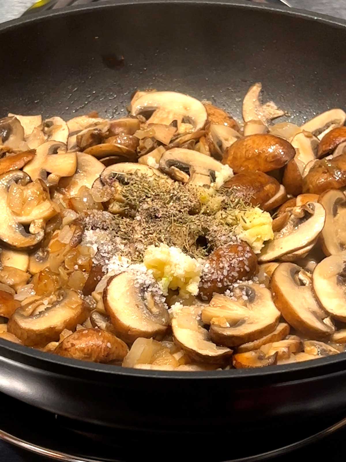 Garlic, salt, thyme and pepper added to cooked onions and mushrooms.