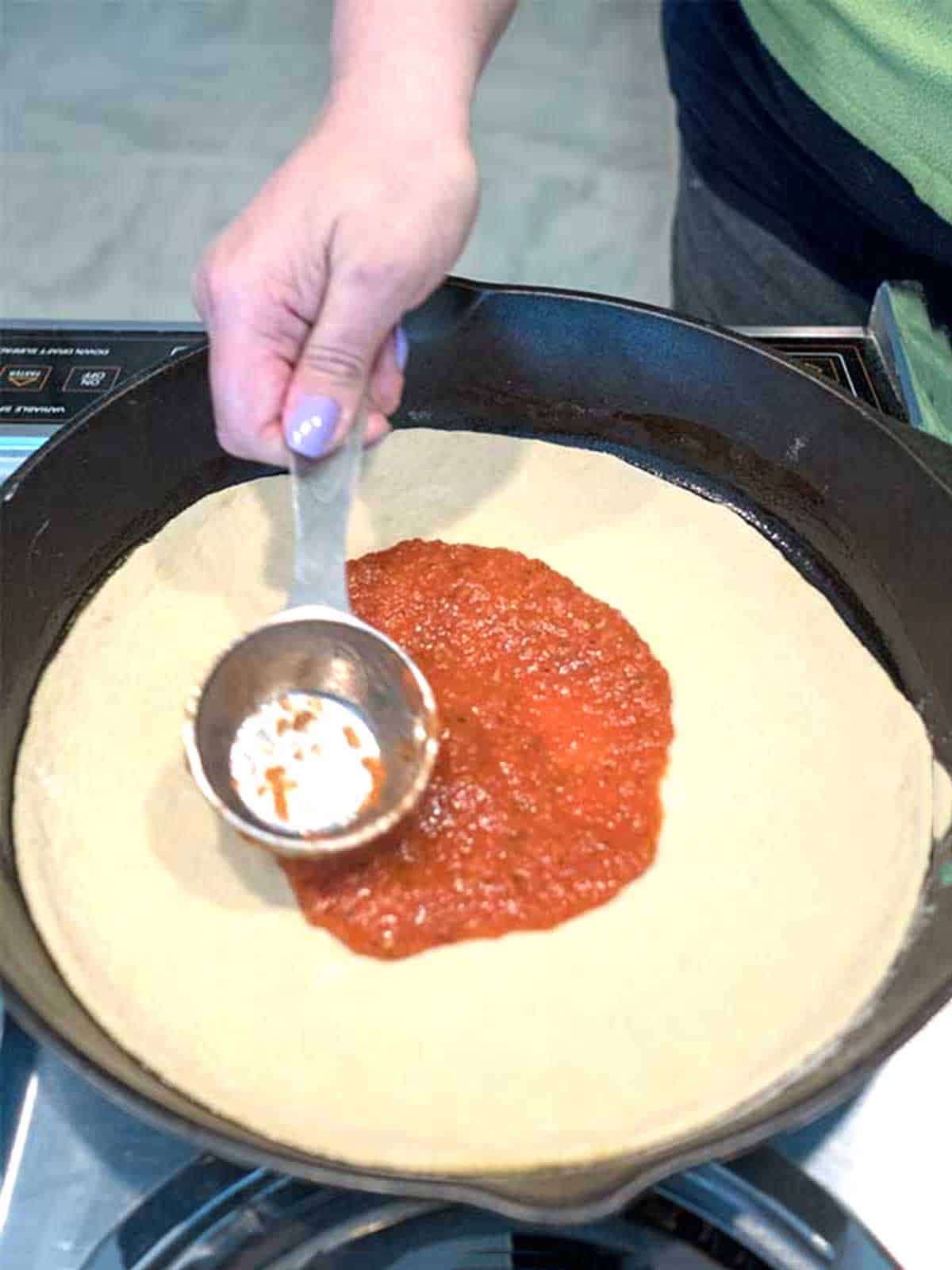 Spreading pizza sauce on dough.