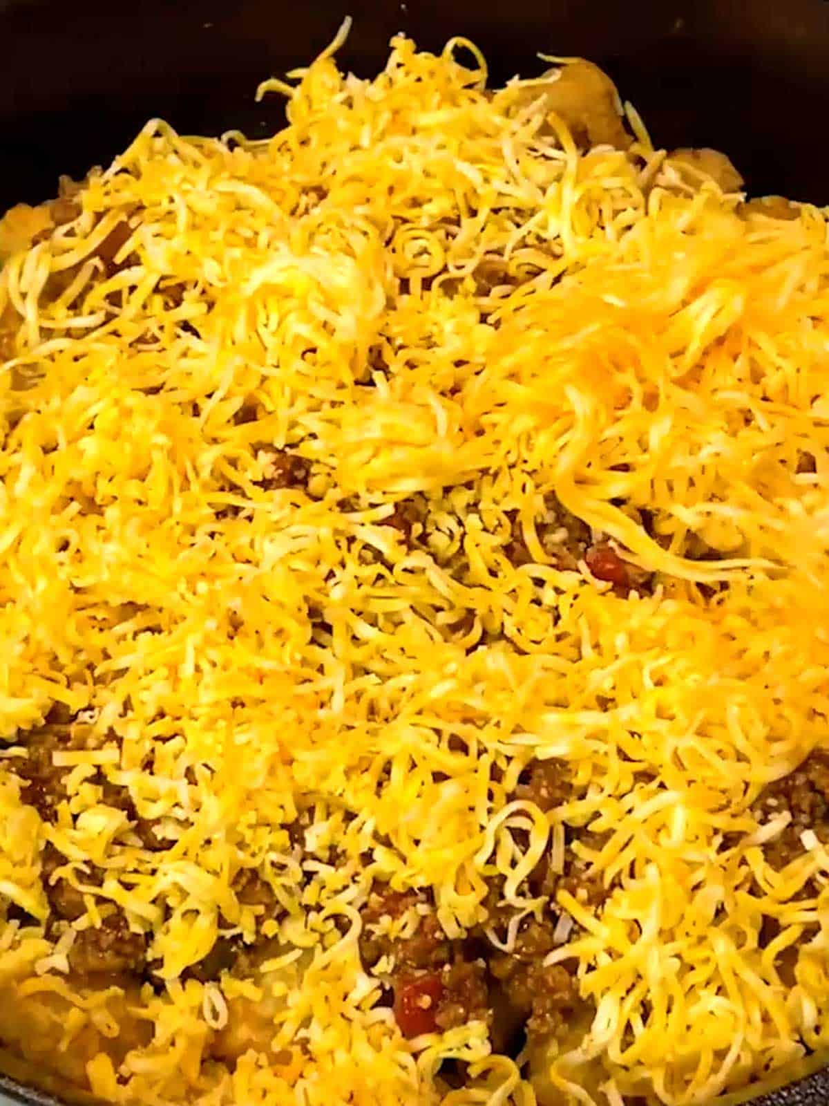 Half of shredded cheese on top of tater tots and taco meat.