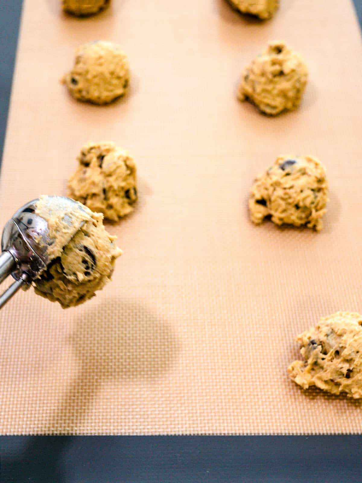 Dropping cookies on silicone lined baking sheet.