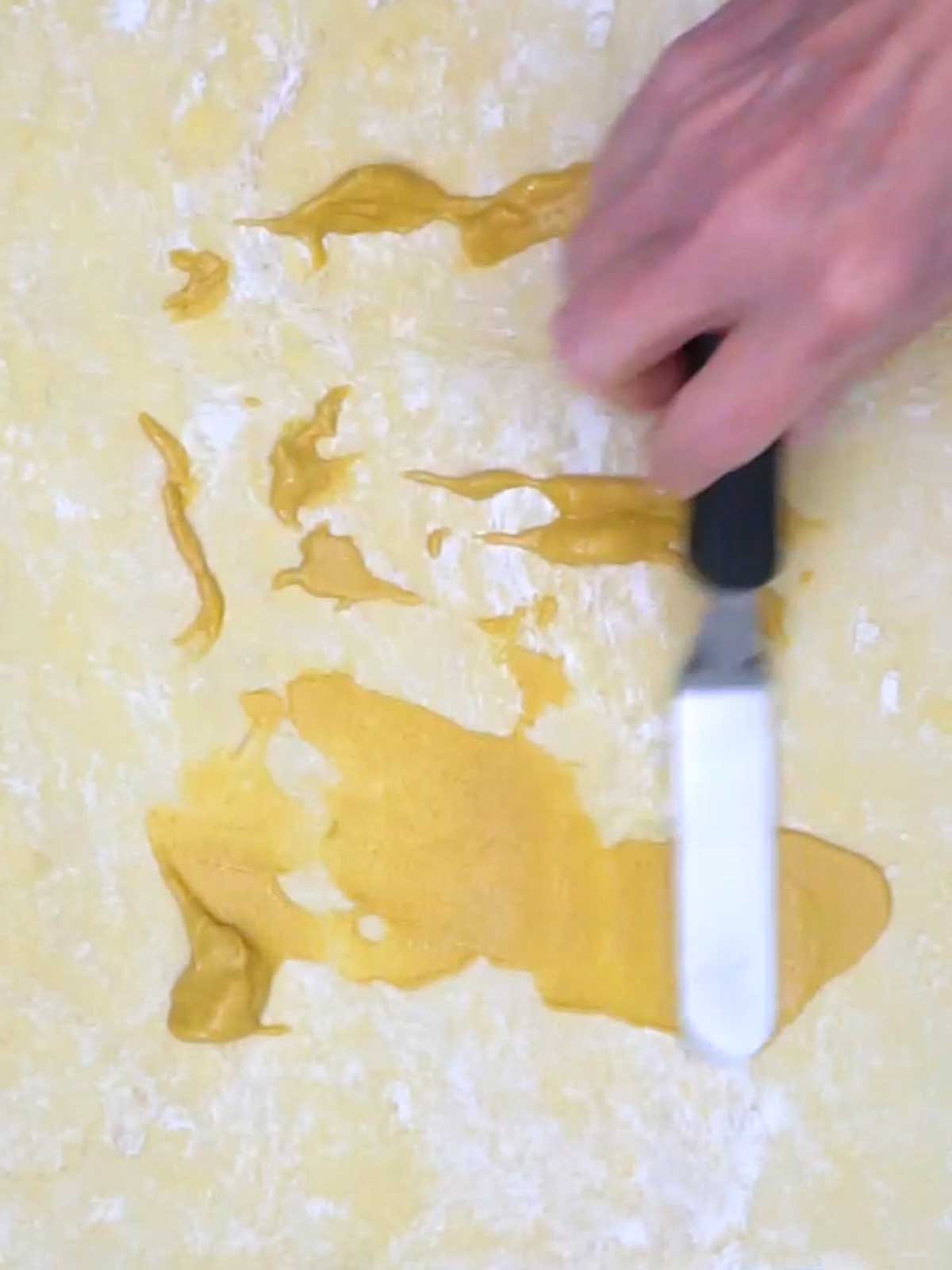 Spreading Dijon mustard on puff pastry sheet.