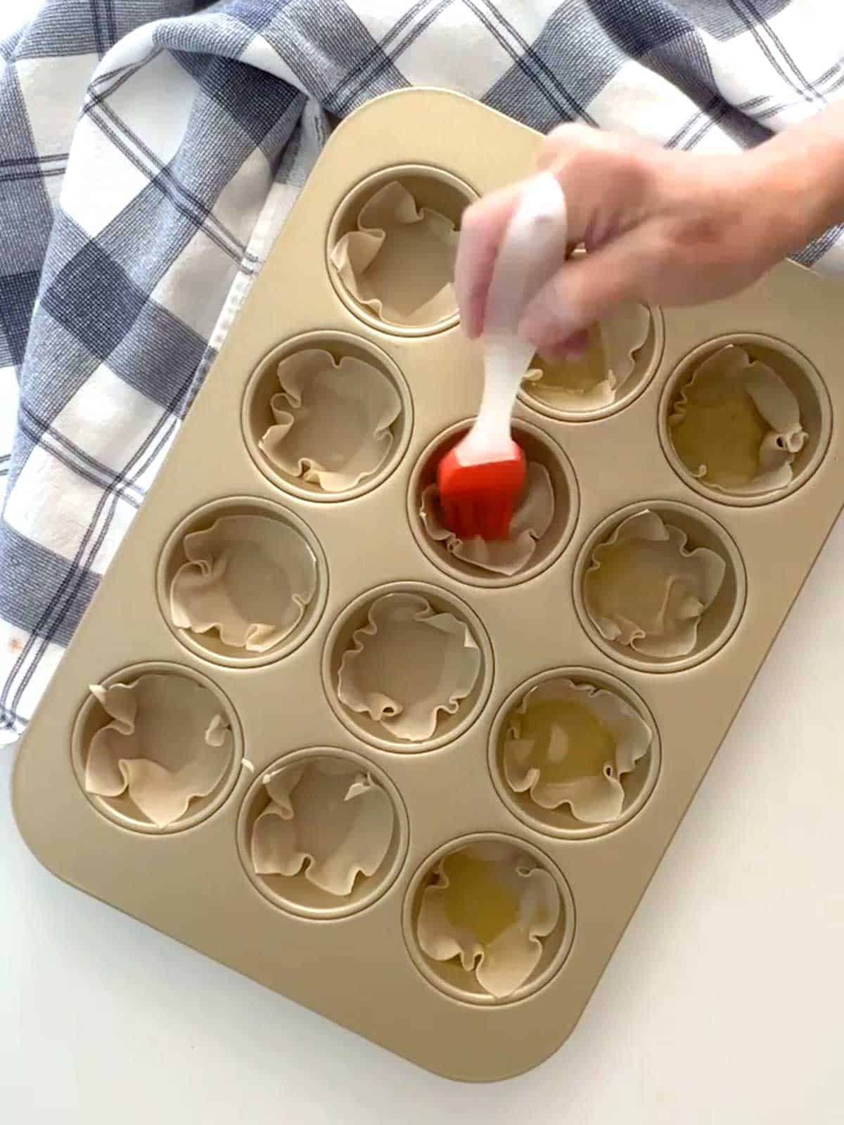 Brushing wontons in muffin pan with olive oil.