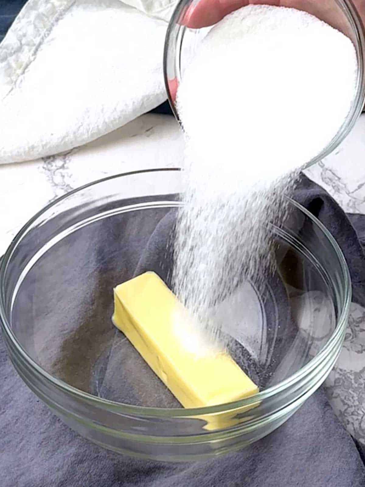 Adding sugar to butter in a bowl.