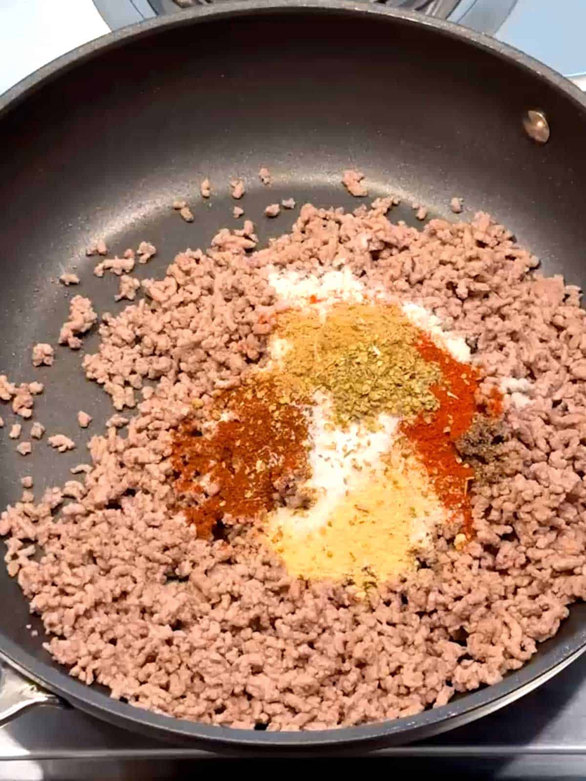 Spices added to browned ground beef in a skillet.