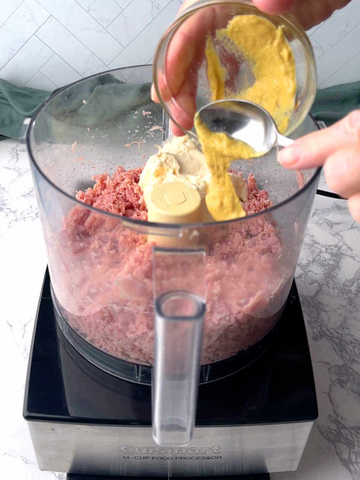 Adding Dijon mustard to the food processor.