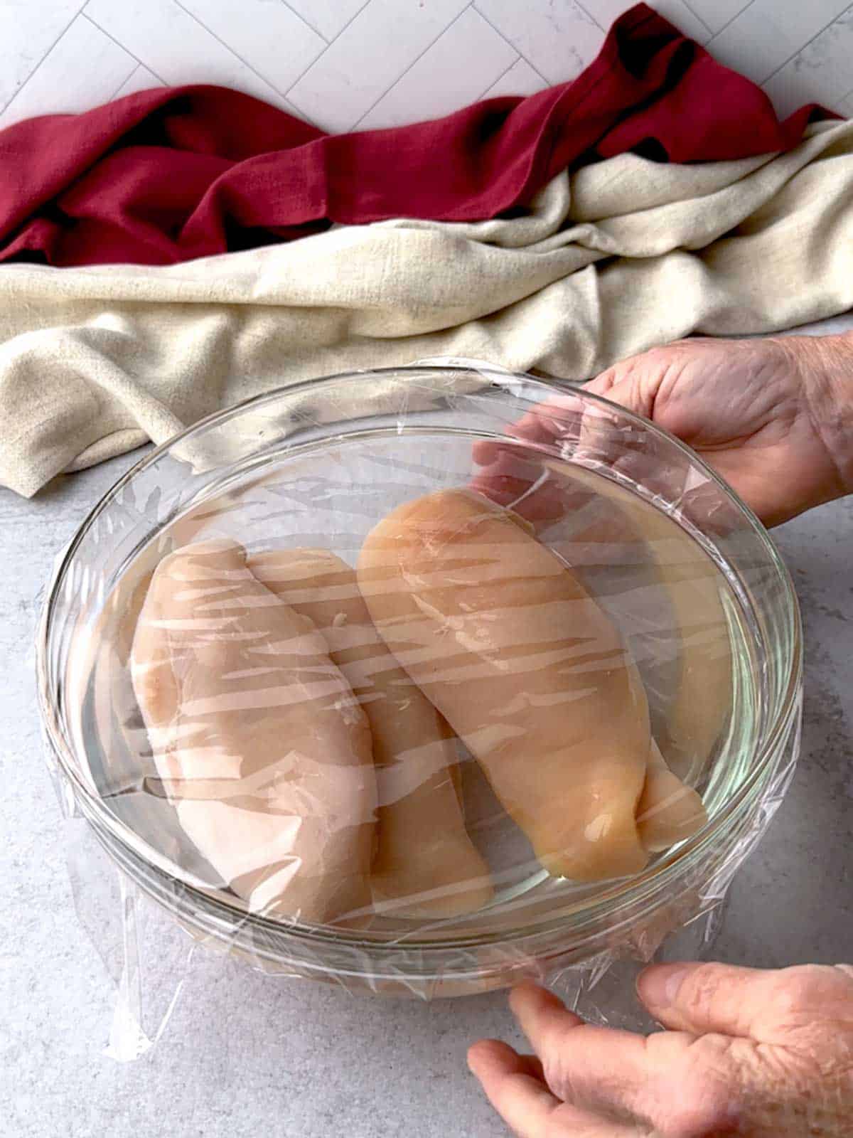 Covering the bowl with the chicken and brining solution with plastic wrap.