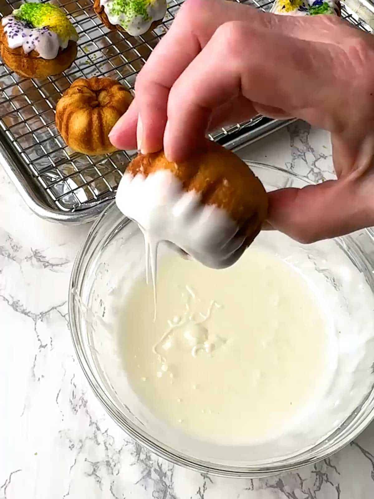 Dipping the little cakes in the frosting and allowing the excess frosting to drip off.