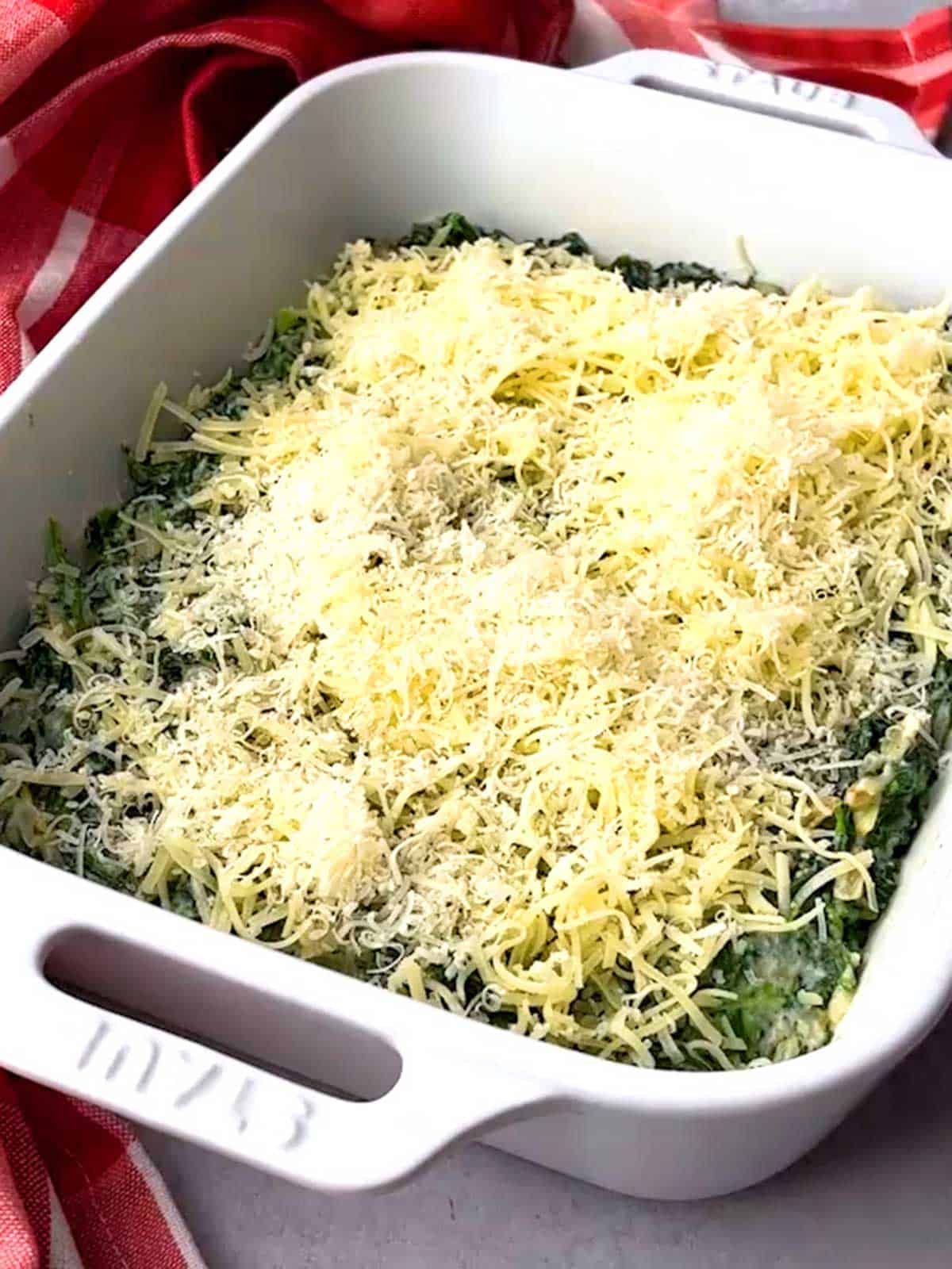Cheese sprinkled on top of spinach gratin in casserole dish.