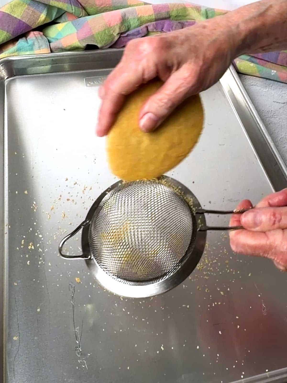 Sanding the edges of the cookie with a wire mesh strainer.