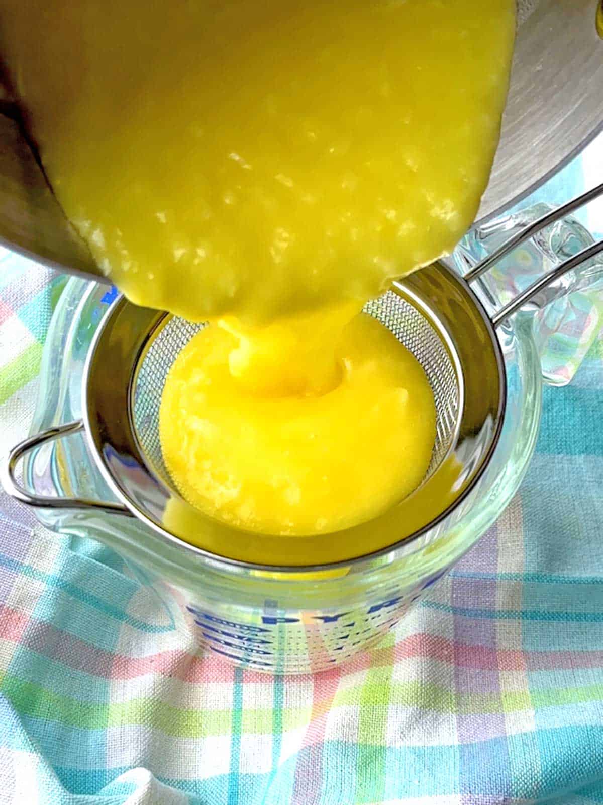 Pouring the lemon curd into a wire mesh strainer set over a measuring cup.